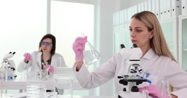 El científico sostiene un frasco con un líquido transparente en sus manos en el laboratorio y observa cuidadosamente. Pruebas de calidad del agua - Metraje, vídeo