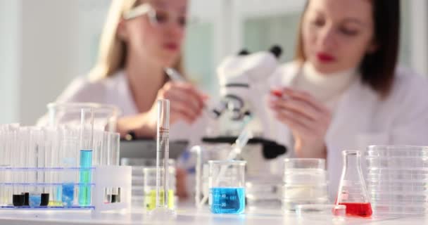 Twee vrouwelijke wetenschappers werken in een laboratorium en een wetenschapper kijkt door een microscoop en een laboratorium assistent druipt vloeibaar. Chemisch medisch onderzoek - Video