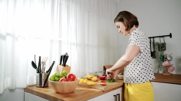 Energetic mother making salad for breakfast at modern kitchen while chopping vegetable surrounded with kitchenware. Smart female house keeper cooking and preparing food. Healthy lifestyle. Pedagogy. - Footage, Video