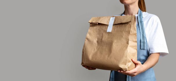 Serveerster houdt bruine pakje tas voor afhaaleten in haar handen. Afhaalmaaltijden online bestellen.  - Foto, afbeelding