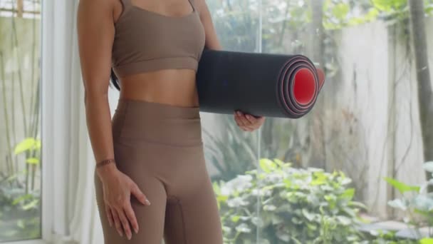 Tilt up portrait of young Asian female athlete holding yoga mat and smiling at camera - Footage, Video