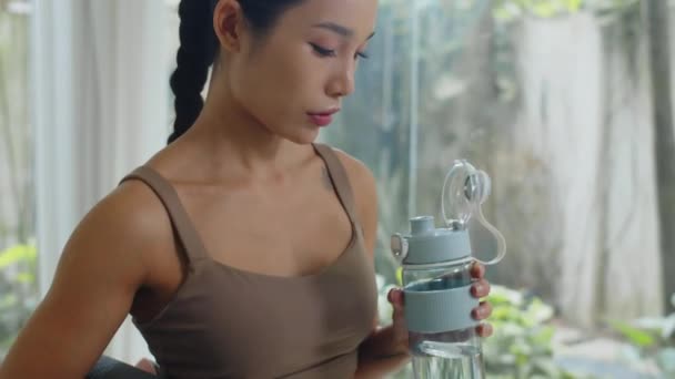 Incline-se tiro de cansaço feminino atleta asiático beber água depois de treinar dentro de casa - Filmagem, Vídeo