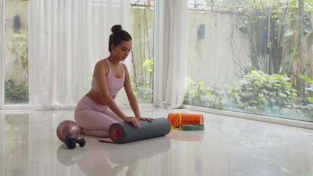 Ampio colpo di giovane asiatica gen Z sportiva rotolamento fuori tappetino yoga mentre si lavora in casa - Filmati, video