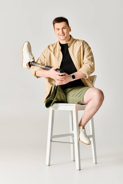 Ein gutaussehender Mann mit Beinprothese sitzt selbstbewusst auf einem weißen Hocker. - Foto, Bild