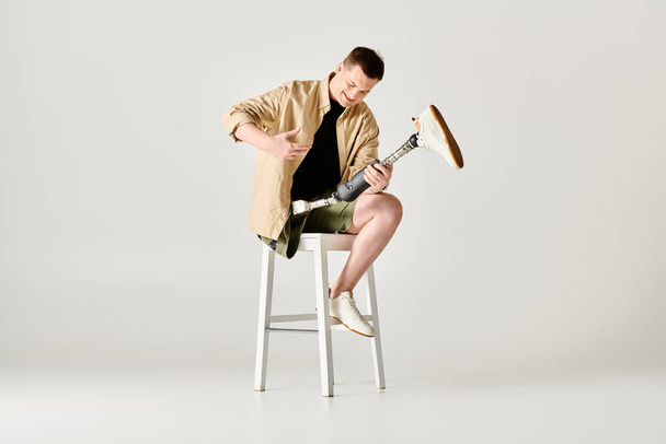 Όμορφος άντρας με προσθετικό πόδι ποζάρει ενώ κάθεται σε σκαμνί.. - Φωτογραφία, εικόνα