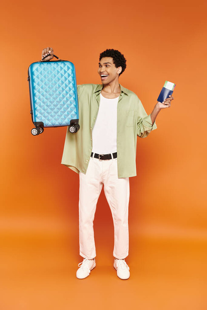 csábító vidám afro-amerikai férfi útlevéllel és jeggyel, és nézi a kék bőrönd - Fotó, kép