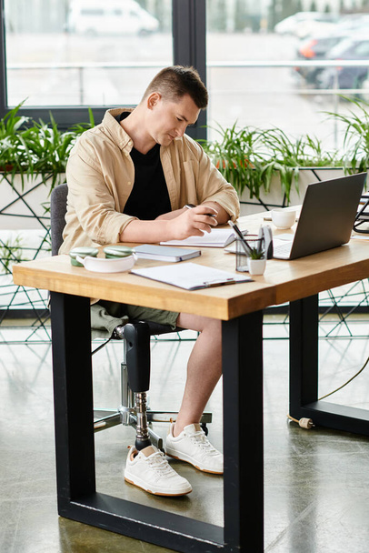 Een knappe zakenman met een kunstbeen werkend aan een laptop aan een tafel. - Foto, afbeelding