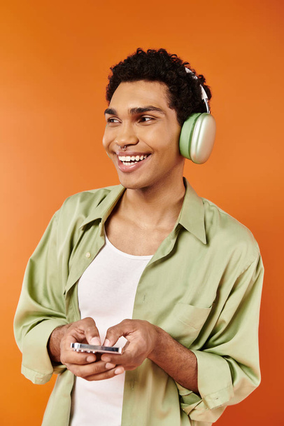 ハッピーな若いアフリカ系アメリカ人男性とヘッドフォンを持って携帯電話を持ち,オレンジ色の背景 - 写真・画像