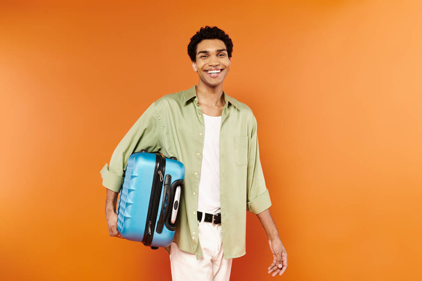 vidám, fiatal afro-amerikai férfi alkalmi ruhában fogja a bőröndjét és mosolyog a kamerába. - Fotó, kép