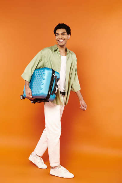 красивий веселий афроамериканський чоловік у затишному одязі, що йде з синьою валізою в руці - Фото, зображення