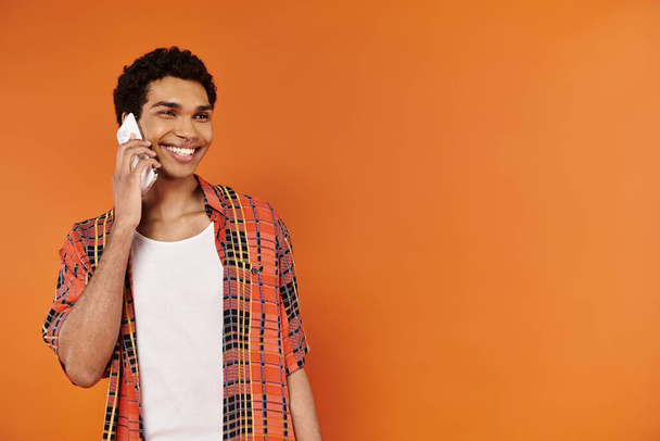 vonzó vidám afro-amerikai férfi élénk ruhát beszél telefonon, és félrenéz - Fotó, kép