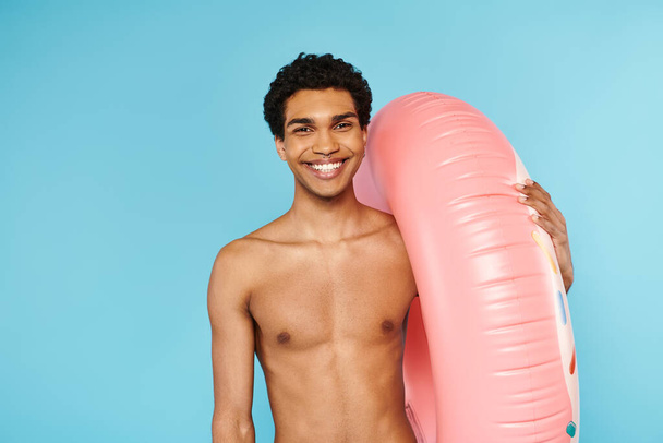 cheerful african american man posing with swimming ring on blue backdrop and looking at camera - Photo, Image