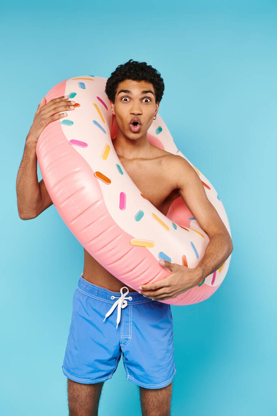 contented african american man posing with swimming ring on blue backdrop and looking at camera - Photo, Image