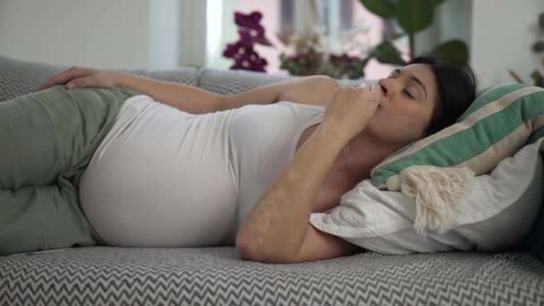 Pensive raskaana oleva nainen makasi sohvalla harkittuja ilme. Äidin pohdiskelu syvässä henkisessä heijastuksessa kattoon tuijottaminen - Materiaali, video