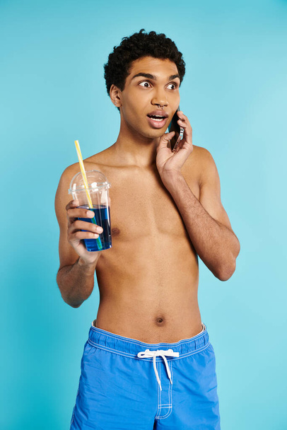 όμορφος Αφροαμερικάνος που μιλάει στο τηλέφωνο και κρατάει ένα δροσιστικό κοκτέιλ στο χέρι του. - Φωτογραφία, εικόνα
