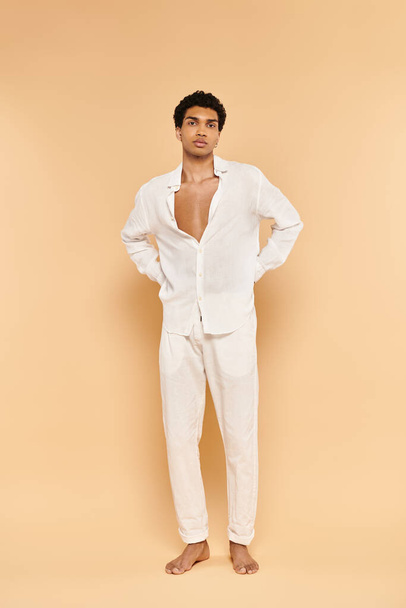 attractive young african american man in white attire posing on beige backdrop and looking at camera - Photo, Image