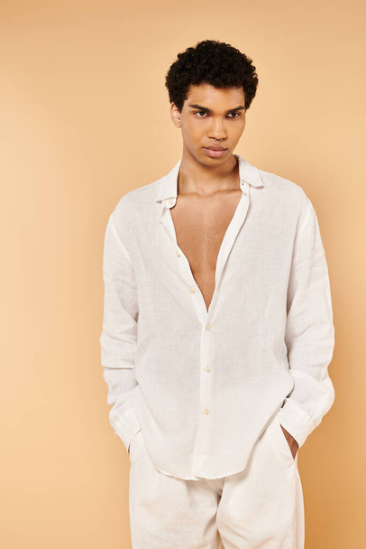 goed gekleed chic Afrikaans amerikaanse man in elegante witte kleding weg te kijken op beige achtergrond - Foto, afbeelding