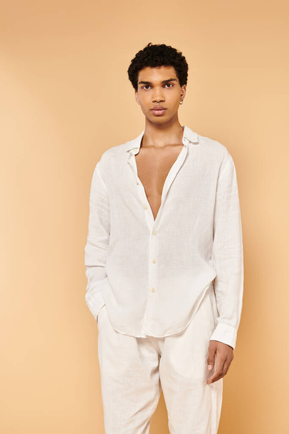 hombre afroamericano bien parecido en traje blanco posando sobre fondo beige y mirando a la cámara - Foto, Imagen