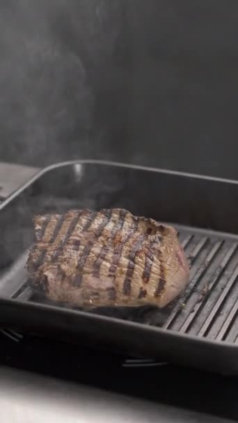 Шеф-кухар готує великий шматочок м'яса на сковороді, наливаючи над ним соус, яловиче рагу з парою на кухні ресторану. Концепція меню гриля. Вертикальний перегляд - Кадри, відео