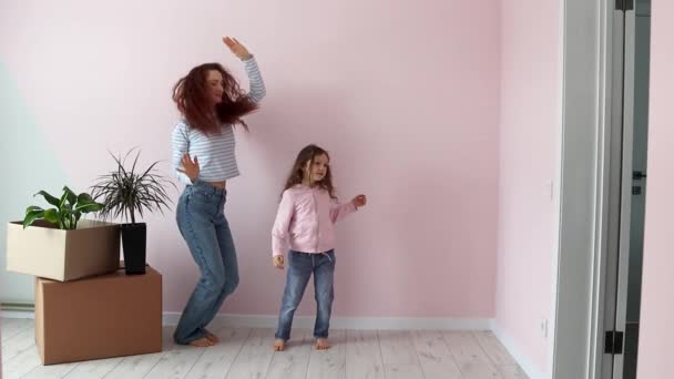 Egy kislány és az anyja boldogan táncolnak a dobozok közelében, örülnek az új otthonuknak. Új lakás. Ingatlan és bérlet, hitel és jelzálog, költözési nap koncepció. Lassú mozgás.. - Felvétel, videó
