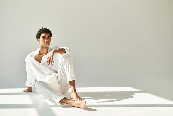 bel homme afro-américain sophistiqué en tenue de lin assis sur le sol et regardant la caméra - Photo, image