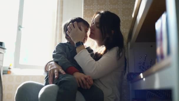 Tarjous hetki keittiössä: poika suutelee äitiään poskelle, heijastaa rakastava suhde ja vahva side vanhemman ja lapsen välillä autenttisessa perhekohtauksessa - Materiaali, video