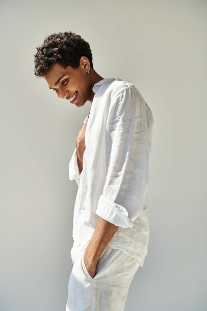 радісна приваблива афроамериканська чоловіча модель в білому лляному вбранні, дивлячись на бежевий фон - Фото, зображення