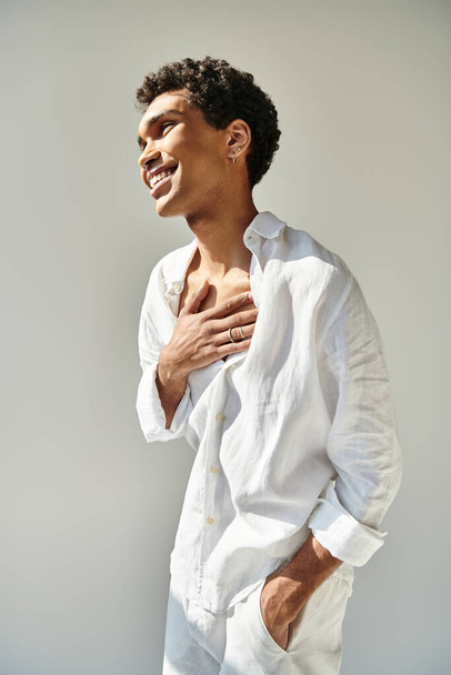 vrolijke verleidelijke Afrikaanse Amerikaanse man model in wit linnen kleding weg te kijken op beige achtergrond - Foto, afbeelding