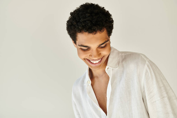 pozitivní svůdný africký americký mužský model v bílém plátně oblečení odvrací pohled na béžové pozadí - Fotografie, Obrázek