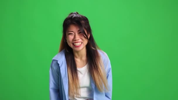 Nuori kaunis aasialainen nainen, opiskelija rento asu nauraa katsellen kamera vastaan elinvoimainen vihreä studio tausta. Ihmisen tunteiden käsite, itseilmaisu, muoti, tyyli. - Materiaali, video