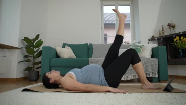 Zwangere vrouw die thuis traint tijdens de late fase van de zwangerschap met Yoga mat die thuis in de woonkamer ligt. Gezondheid en welzijn tijdens de prenatale praktijk - Video