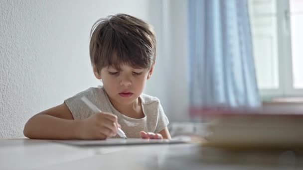 Mały chłopiec w swoim pokoju, doskonalił swoje umiejętności pisma ręcznego w swoim biurku - Materiał filmowy, wideo