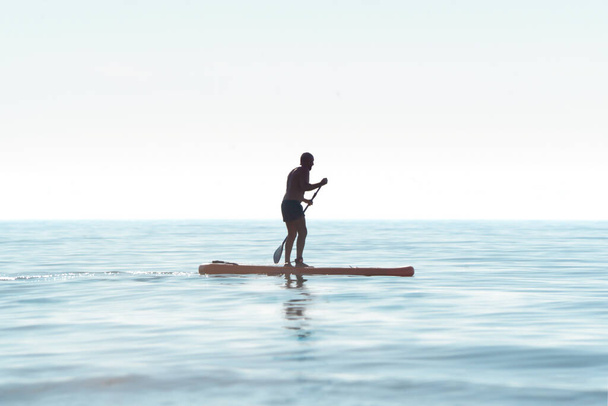 Σιλουέτα ενός καγιάκ σε μια προσωπική κωπηλασία καγιάκ, κωπηλασία ένα καγιάκ με ένα κουπί στα ήρεμα νερά του ωκεανού την αυγή. Καλοκαιρινές αθλητικές διακοπές στη θάλασσα - Φωτογραφία, εικόνα