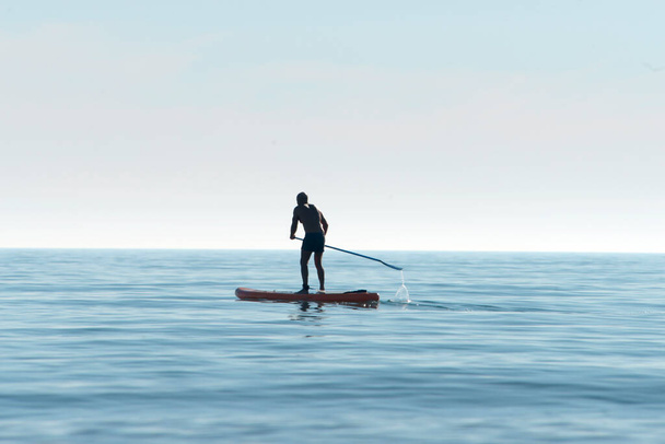 Силует каяка на особистому веслувальному каяку, веслуючи на каяку з веслами у спокійних водах океану на світанку. Літній спортивний відпочинок на воді в морі - Фото, зображення