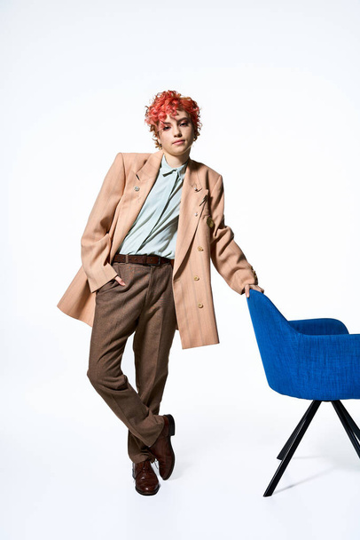 Straordinaria donna con i capelli rossi si erge con fiducia accanto a una sedia. - Foto, immagini
