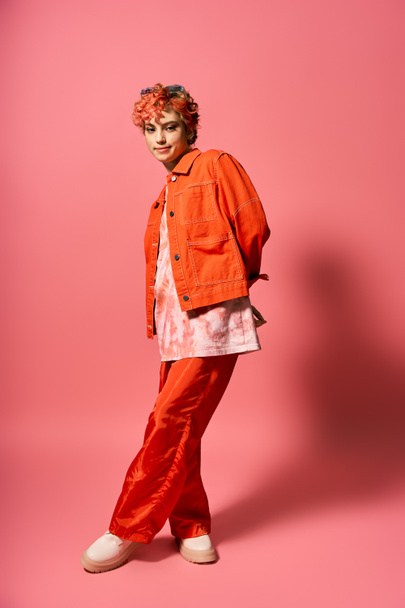 Stylowa kobieta w pomarańczowej kurtce i czerwonych spodniach. - Zdjęcie, obraz