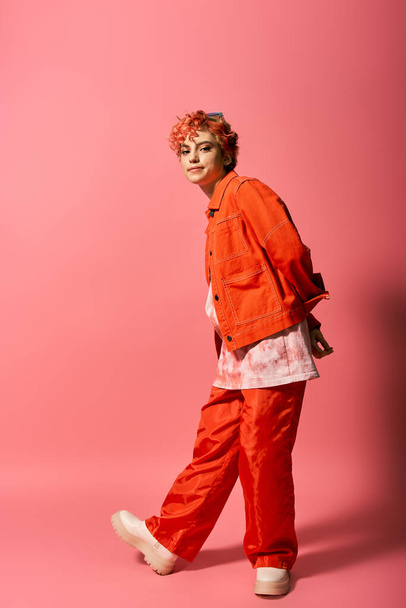 Необыкновенная женщина в оранжевой куртке и красных штанах выделяется на ярком фоне. - Фото, изображение