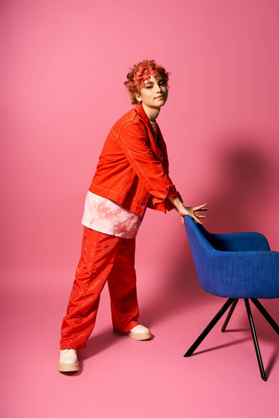 Femme extraordinaire en costume rouge poussant une chaise bleue vibrante. - Photo, image