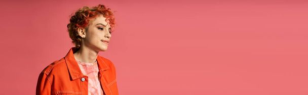 Μια γυναίκα με πορτοκαλί σακάκι με αυτοπεποίθηση ξεχωρίζει σε ένα ζωντανό ροζ φόντο. - Φωτογραφία, εικόνα