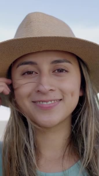 Vídeo HD vertical de joven mujer latina sonriente en sombrero de verano mirando a la cámara al aire libre. Imágenes en cámara lenta, expresión positiva. Pueblo hondureño. - Imágenes, Vídeo