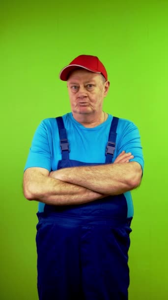 Senior man in in overalls says no, sign disapproval looking at camera. Mature person showing denying, rejecting, disagree. Green screen. Chroma key. Vertical. - Footage, Video