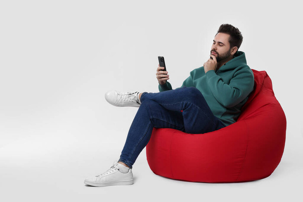 Handsome young man using smartphone on bean bag chair against white background, space for text - 写真・画像