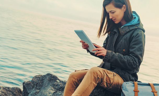 Traveler girl sitting on coast with tablet - Zdjęcie, obraz