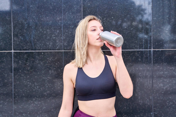 junge blonde Frau im sportlichen Top Trinkwasser auf neutralem Hintergrund - Foto, Bild
