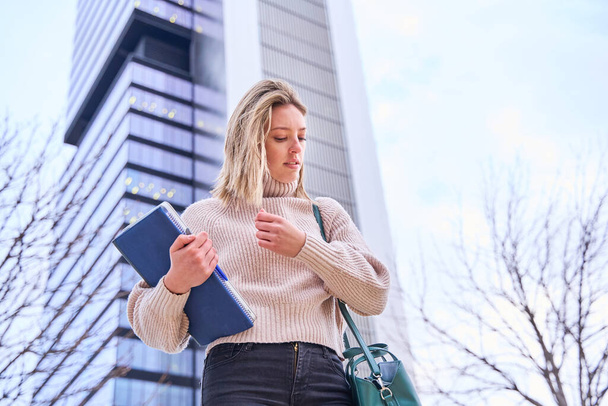 portret van een vrouwelijke universiteitsstudent met boeken en notitieboekjes in haar hand staand op de universiteitscampus. - Foto, afbeelding