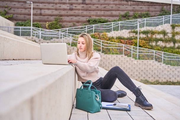 студентка, использующая ноутбук компьютер современные технологии устройства на открытом воздухе в университетском кампусе онлайн обучения, обучаясь снаружи сидя на городской лестнице. Концепция веб-курсов обучения. - Фото, изображение