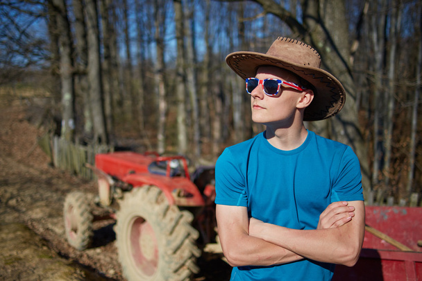 Cowboy teenager standing near the tractor - Фото, изображение