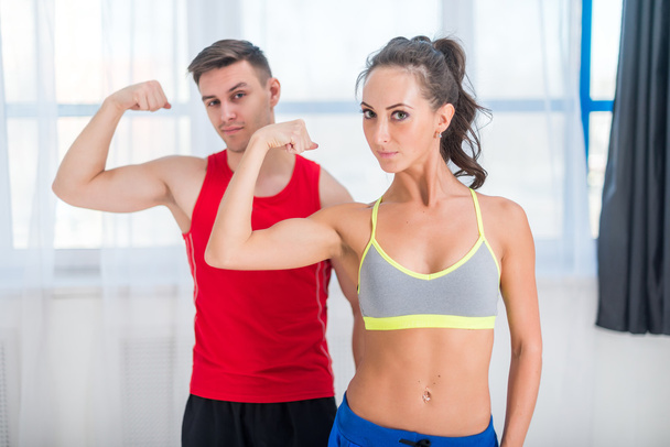 Actieve atletische sportieve vrouw meisje en man tonen hun spieren biceps gezonde levensstijl camera kijken - Foto, afbeelding