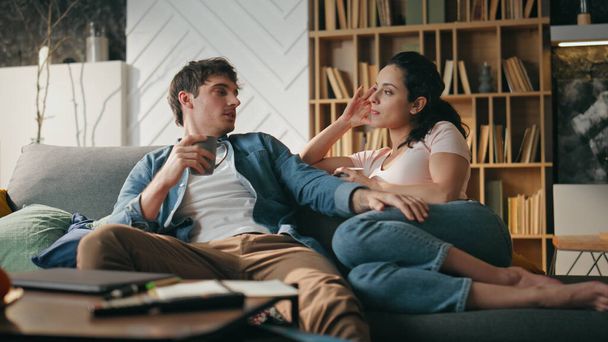 Couple talking in cozy living room sitting comfortable couch. Bonding spouses enjoy pleasant conversation holding coffee cup at home. Young happy family speaking sharing thoughts dreams plans together - Photo, Image