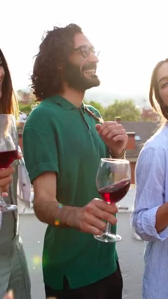 Joven grupo de amigos divirtiéndose brindando por el vino tinto mientras bailan juntos en la fiesta del atardecer en la azotea. Imágenes 4K en cámara lenta. - Metraje, vídeo